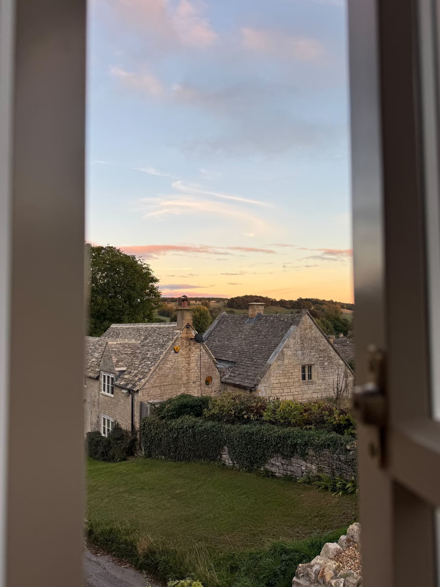 Stone cottages and rooftops at sunset through an open window